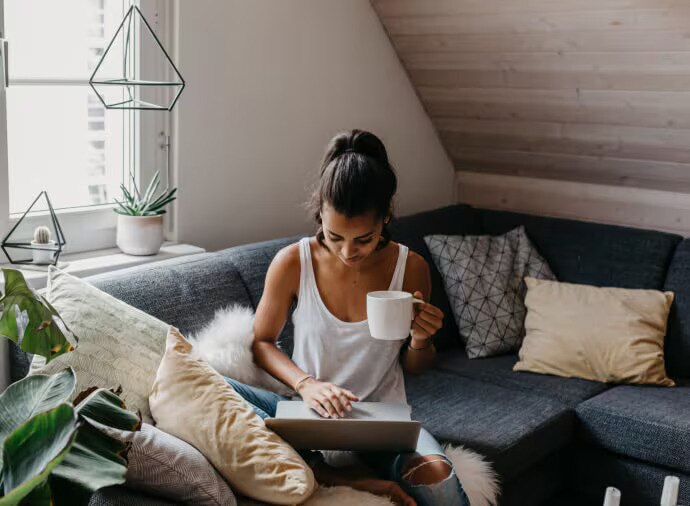 Woman with mug sitting on couch with a laptop